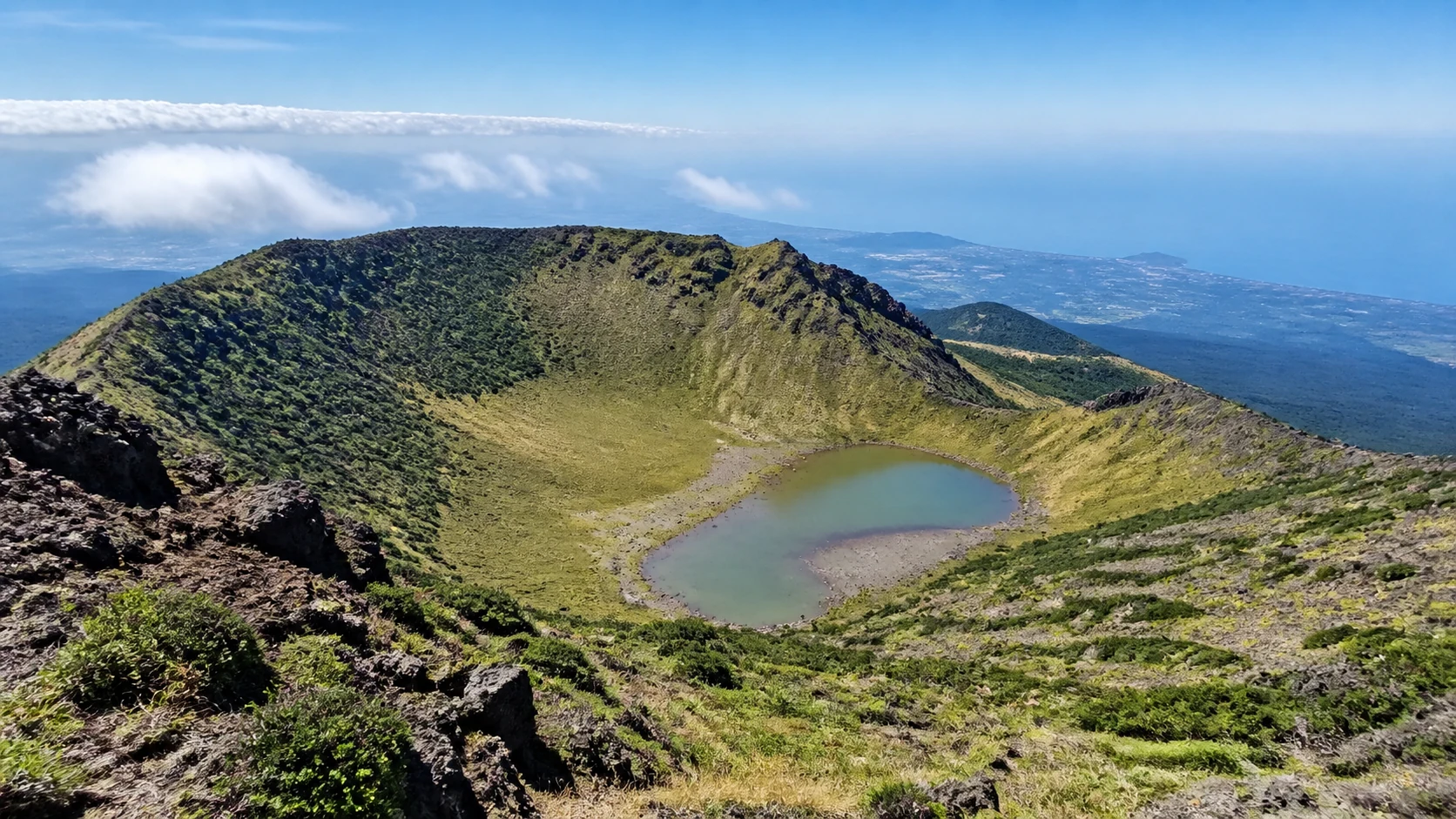 漢拏山山頂の火口壁と白鹿潭の火口湖、その向こうに広がる済州島と海